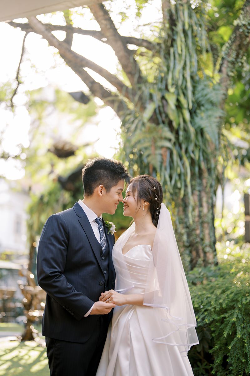 A romantic wedding photoshoot in a garden setting with natural sunlight filtering through trees.
