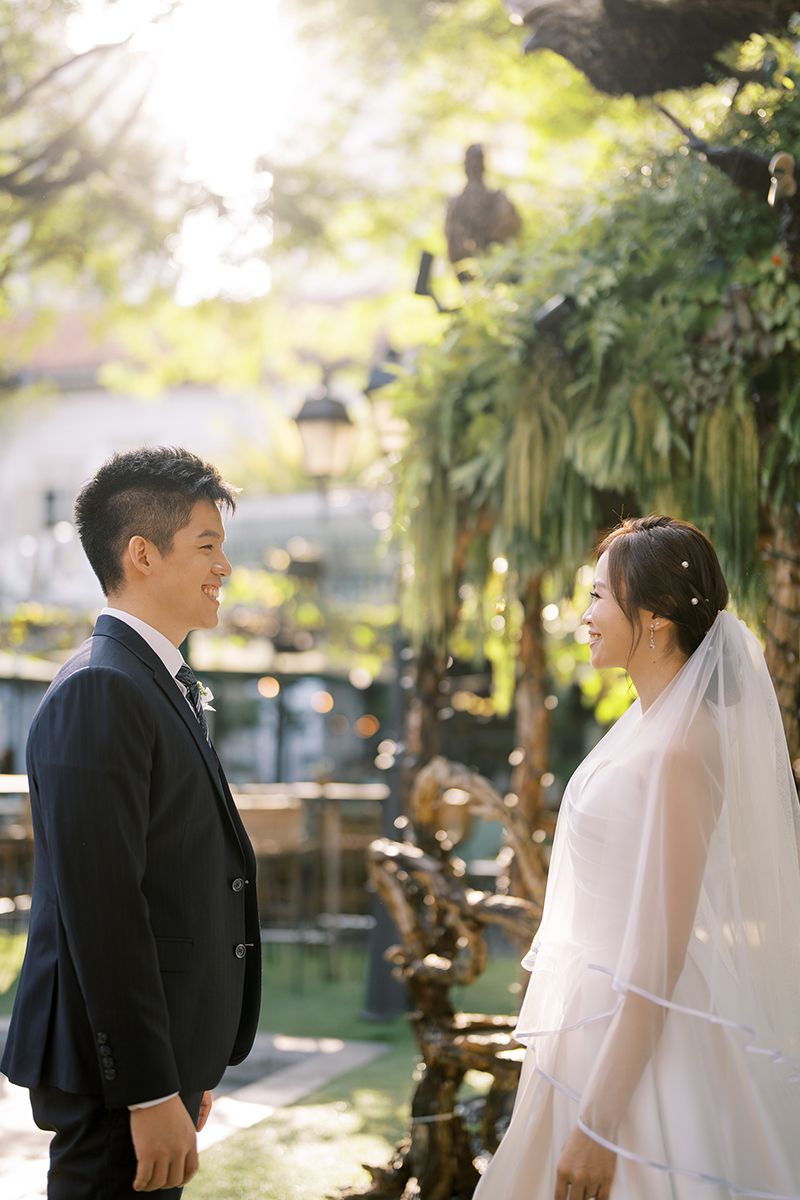 Wedding photos captured in a sunlit garden with tropical plants and trees in the background.