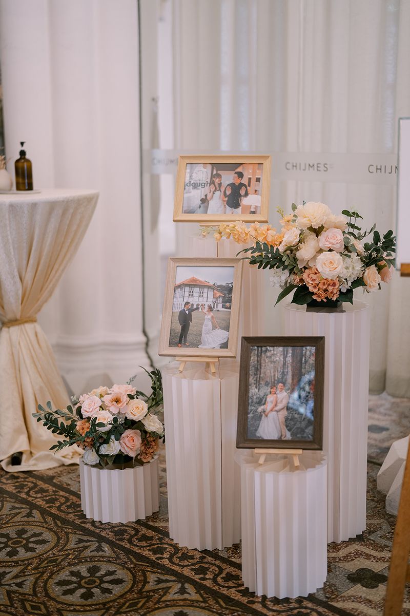Wedding reception setup with white columns, delicate floral arrangements, and photo displays on ornate carpet.