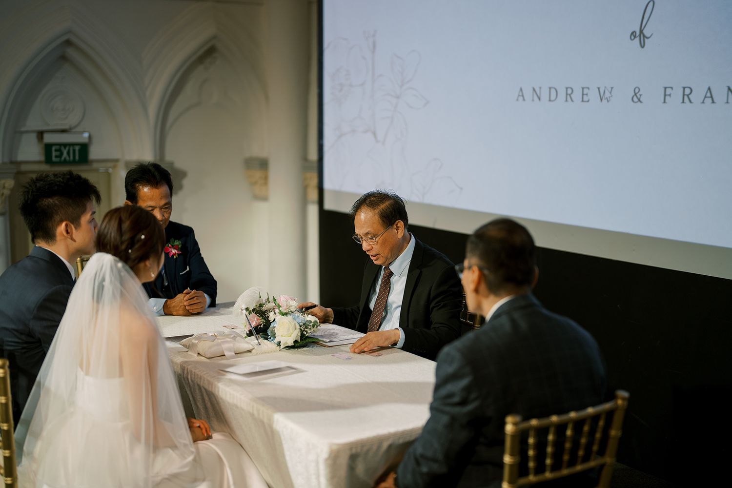 Wedding guests seated at tables in an elegant white venue during a reception celebration.