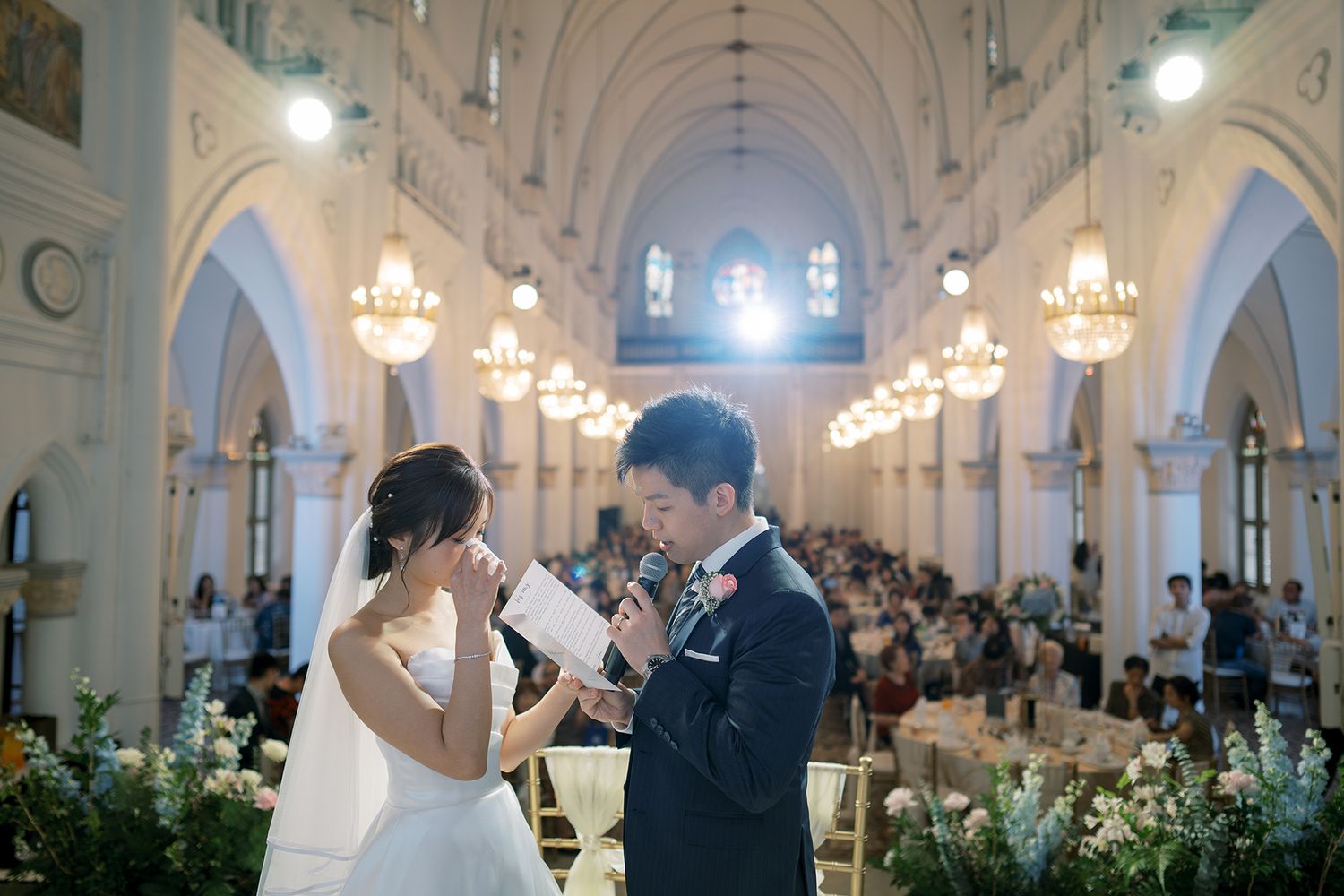 Traditional church wedding ceremony taking place in a beautiful cathedral with arched ceilings and chandeliers.