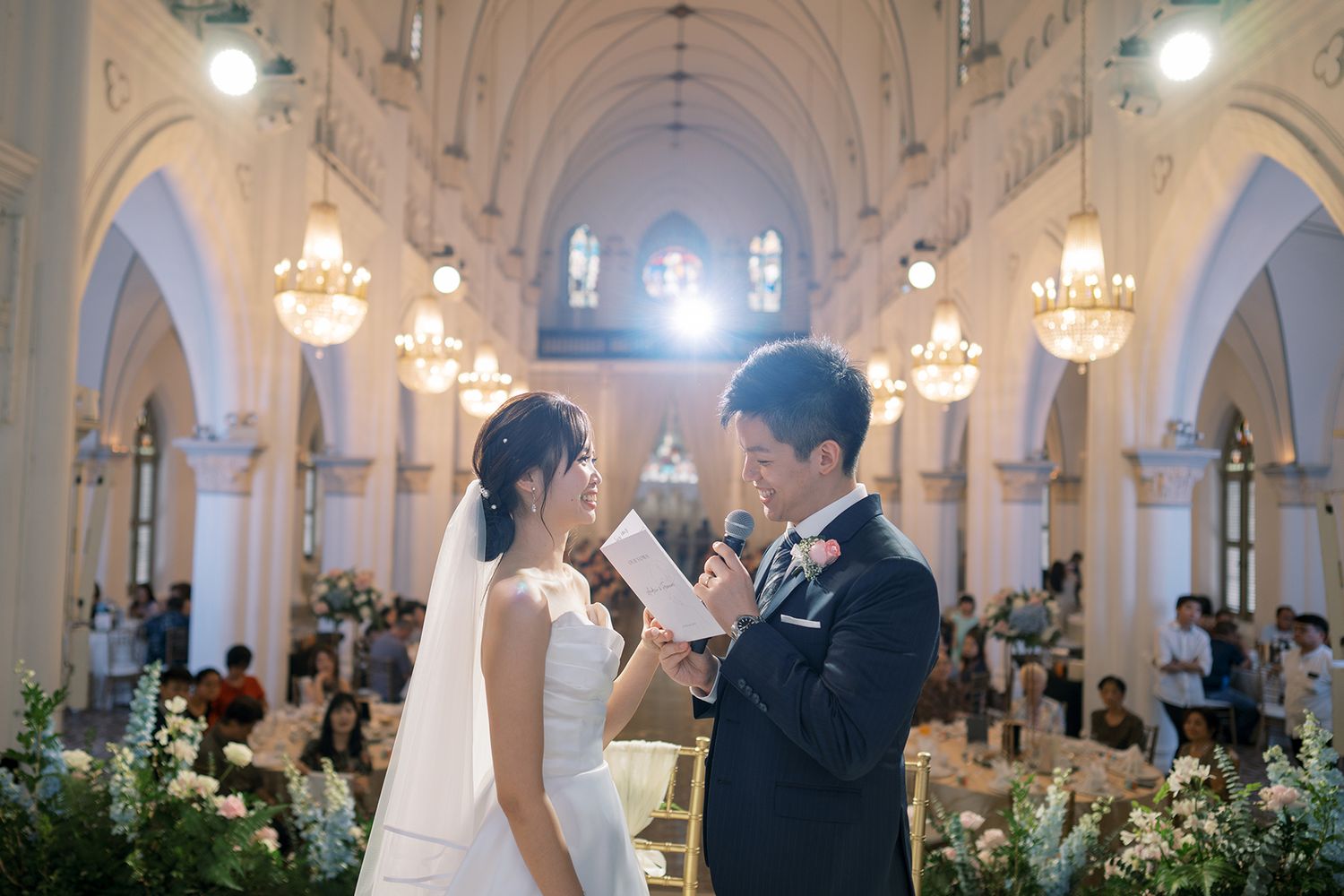 Wedding ceremony in a grand cathedral with ornate architecture and glowing chandeliers.