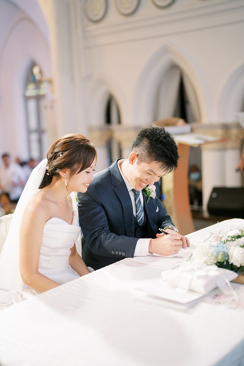 Wedding couple signing documents at a white-clothed table during their ceremony.