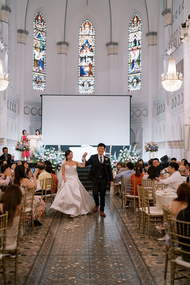 Church wedding reception space with gold chairs and stained glass windows illuminating the room.