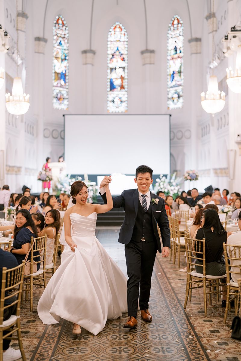 Wedding ceremony in a grand church with stained glass windows and gold chiavari chairs lined up in rows.