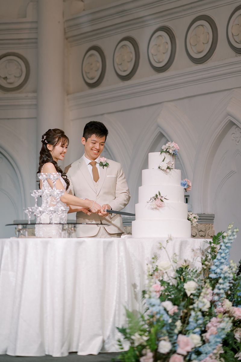 Wedding cake display with floral decorations on a white tablecloth in an elegant venue.