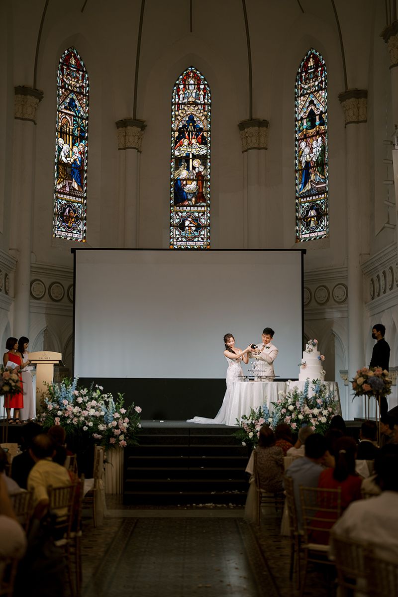 Church wedding ceremony with stained glass windows and floral arrangements on the altar.