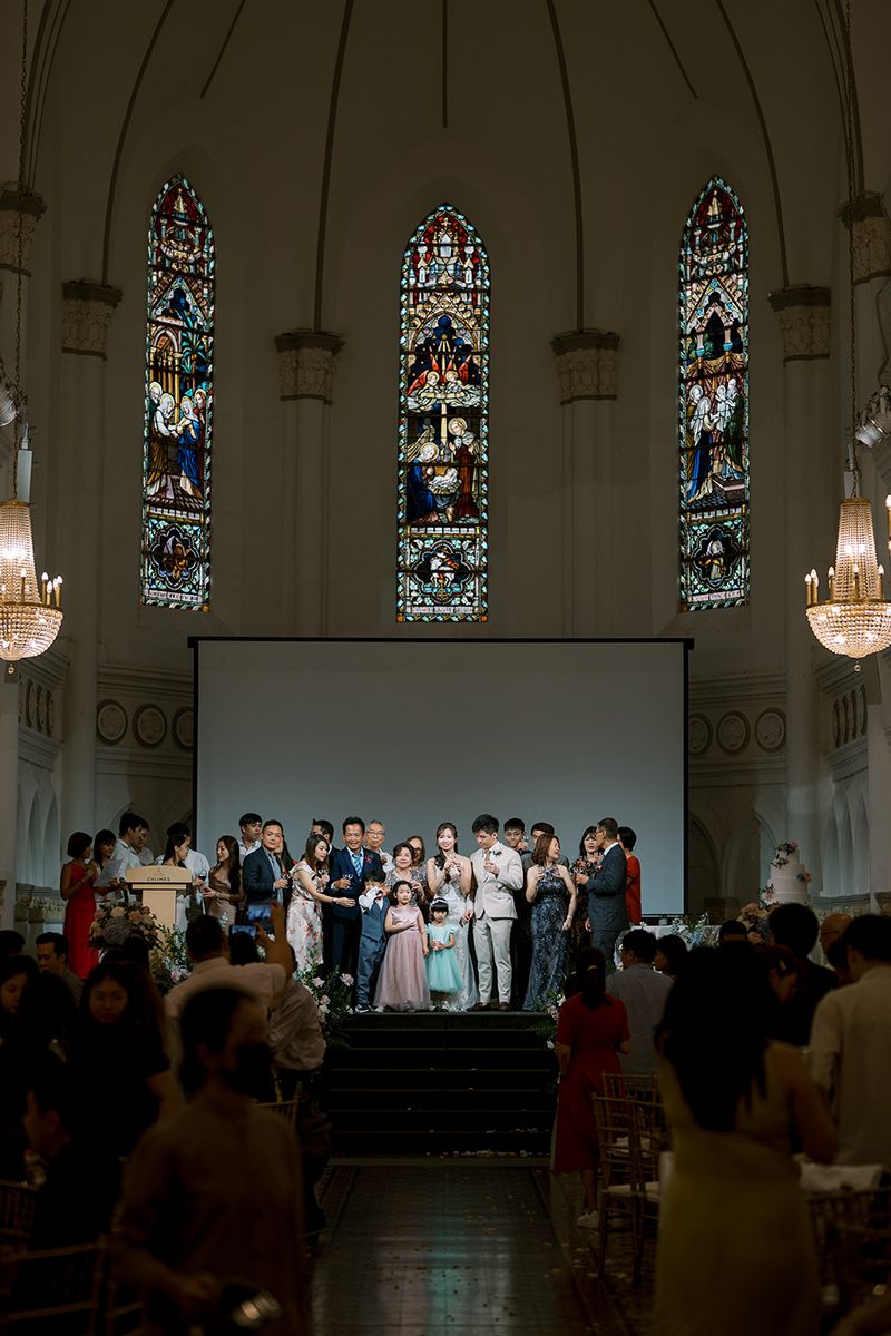 Wedding celebration in a historic church with stained glass windows and chandeliers overhead.