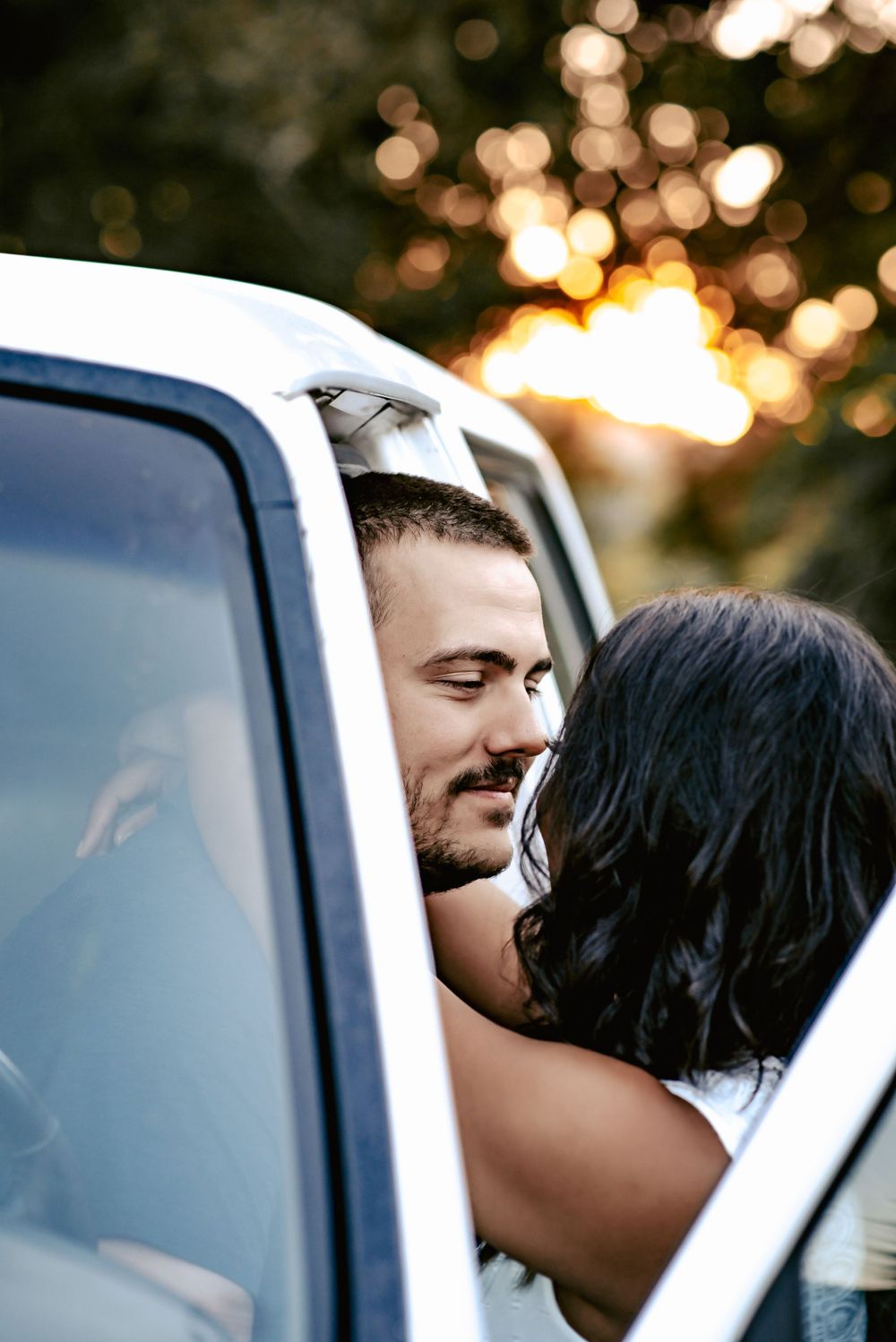 A couple shares an intimate moment near a car door during golden hour sunset.