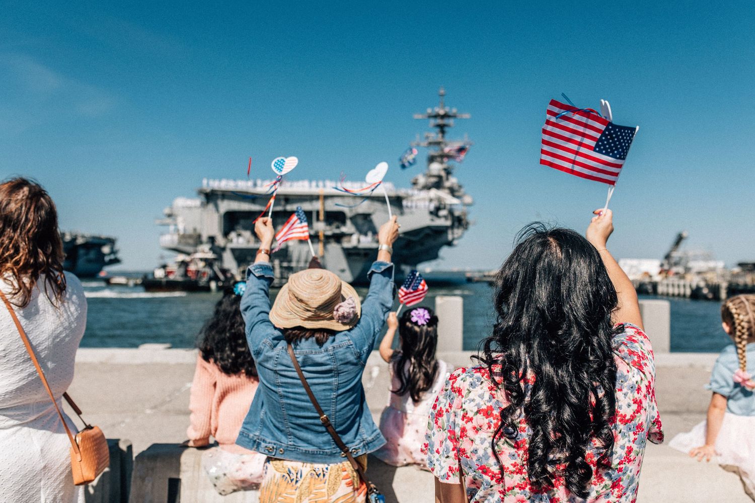 family holding and waving flags as they welcome home a ship in norfolk, virginia