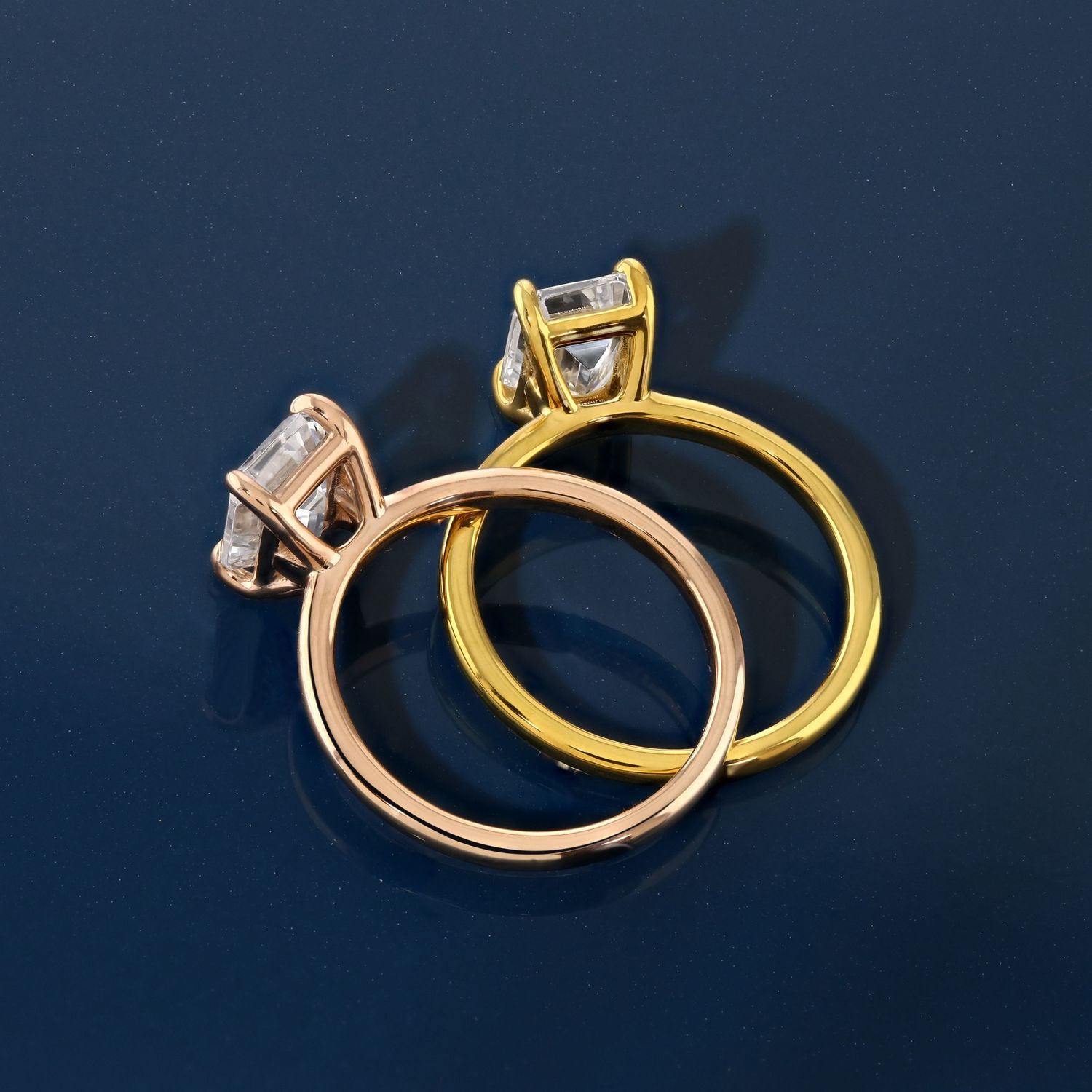 Rose gold and yellow gold solitaire engagement rings against navy blue background.