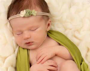 Newborn Photo shoot, baby wrapped in stretch green wrap, with matching cream & Green newborn flower tieback.
