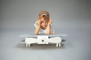 child portrait on wooden grey & white aeroplane photo prop, backdrop grey/wearing pilot hat & goggles