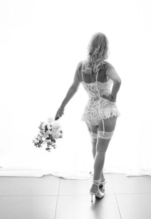 Boudoir Bride, model wearing white lace Basque, stockings & suspenders holding bridal bouquet