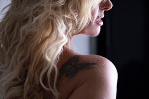 blonde female boudoir shoot, butterfly tattoo on shoulder, model lip stud piercing