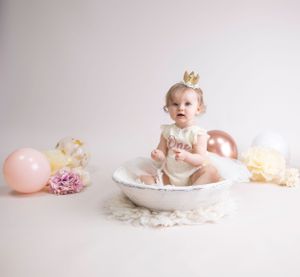 1 year sitter session, cream backdrop, rose gold balloons pink flowers & balloons child wearing cream lace/ribbon Dress