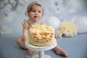 girls cake smash photo shoot blue floral backdrop white cake stand white balloons and cream flowers