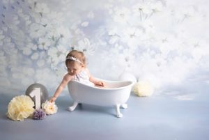 1 year cake smash, Victorian bath, child wearing lilac lace body suit cream grey white flowers/balloons wooden no.1