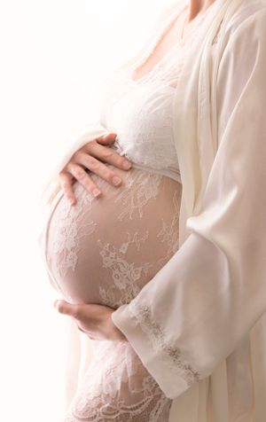 Elegant Maternity Back Lit Image,  Side view of bump, mum to be wearing lace teddy with silk, lovingly cradling her bump