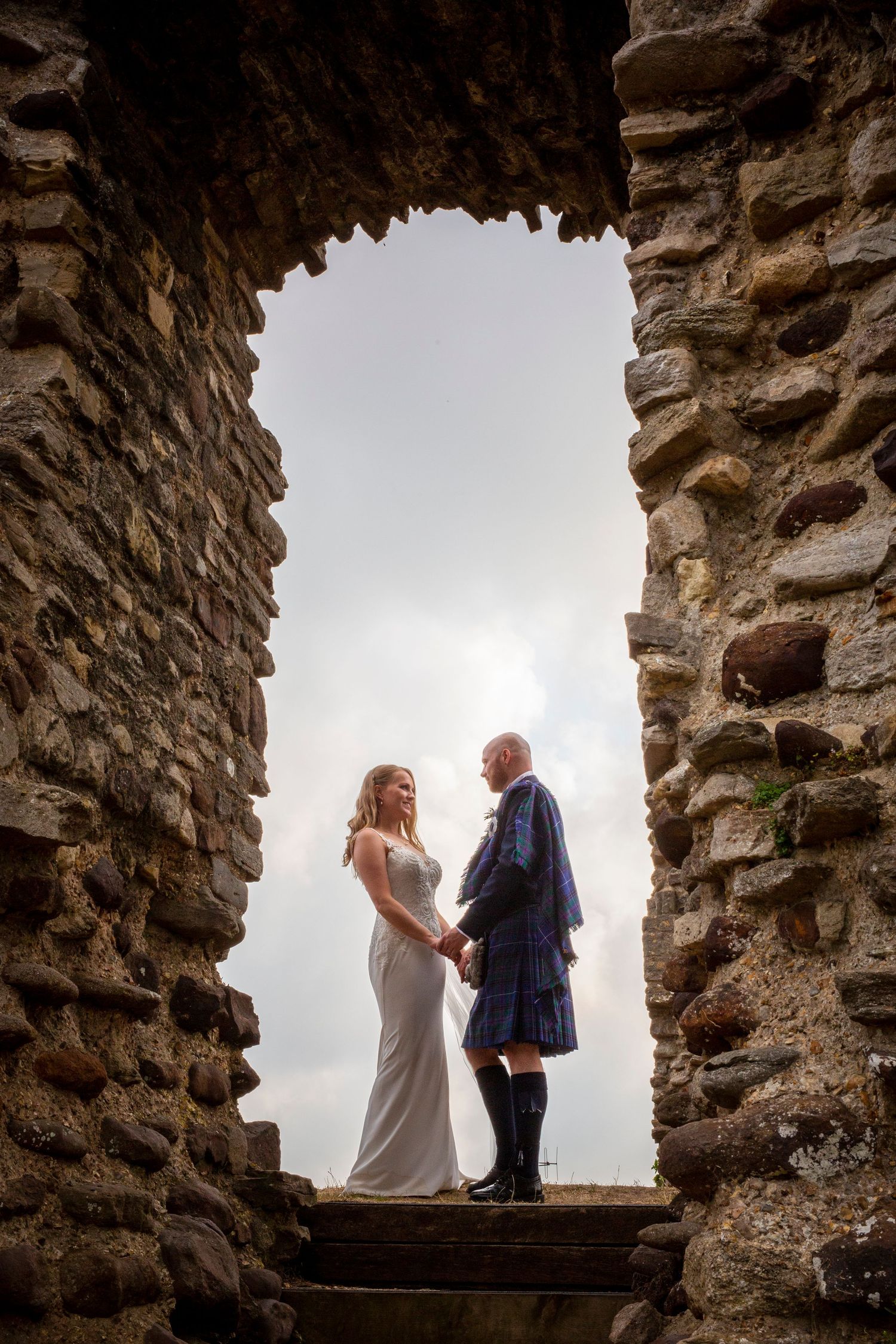 Romantic couple framed within stone castle window against cloudy sky.