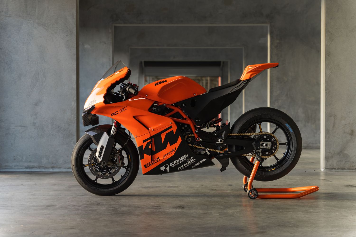 Bright orange racing motorcycle displayed in a concrete showroom space.