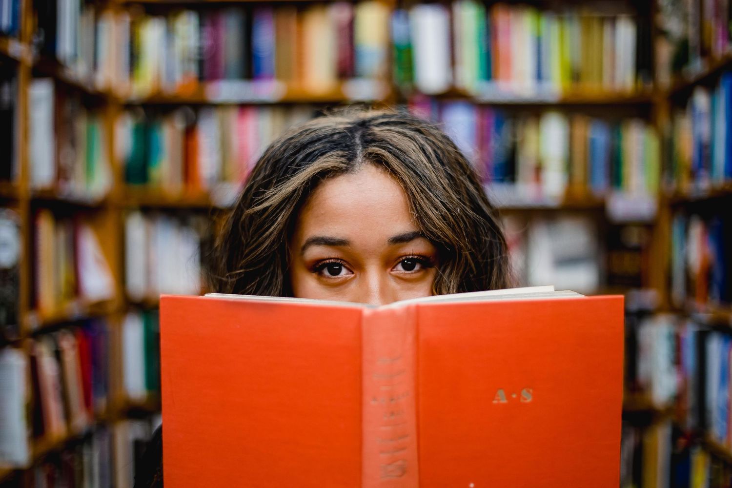 Girl peeking her eyes from behind an orange book at a bookstore