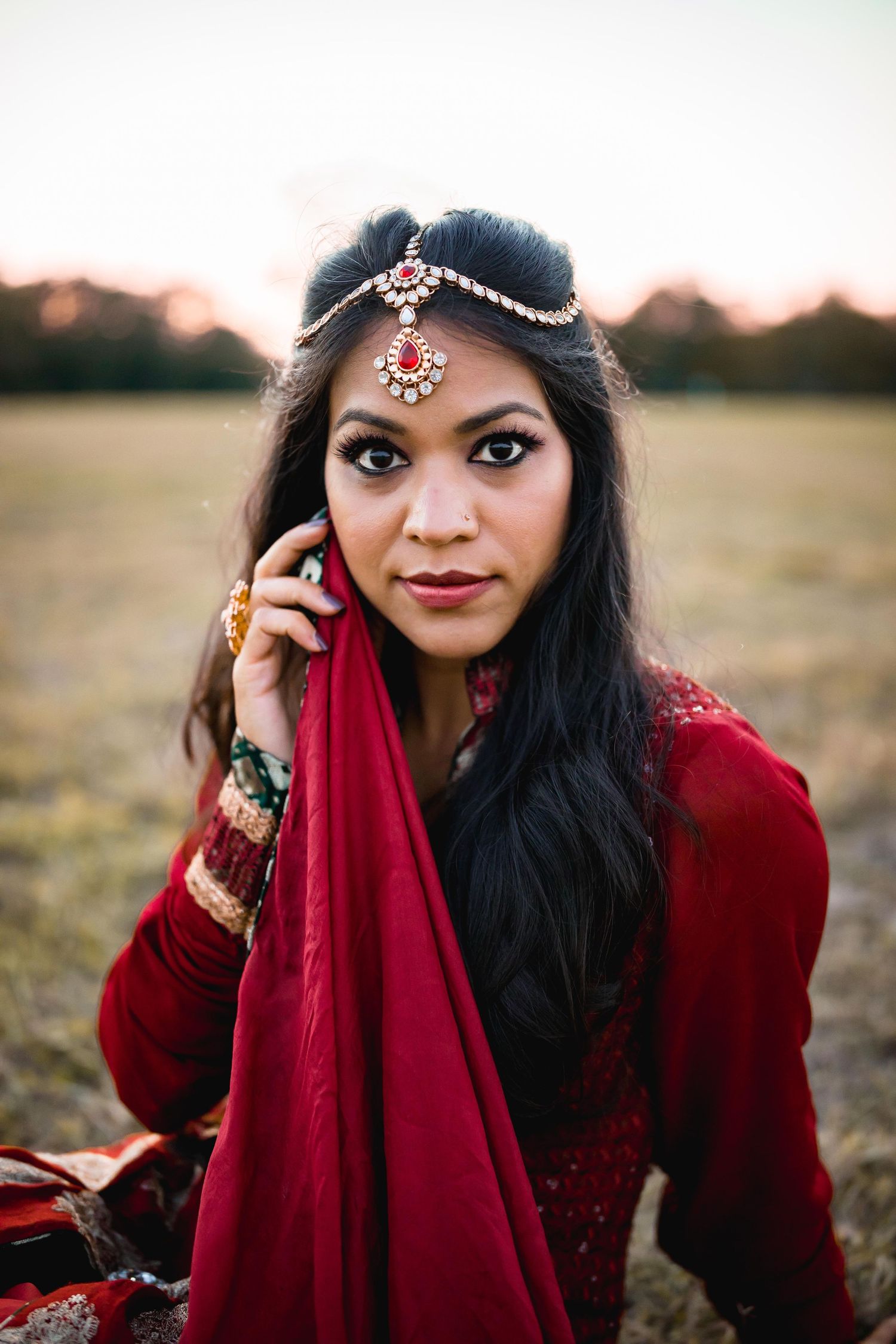 Indian woman wearing traditional dress holding red scarf up to face, Bollywood inspired