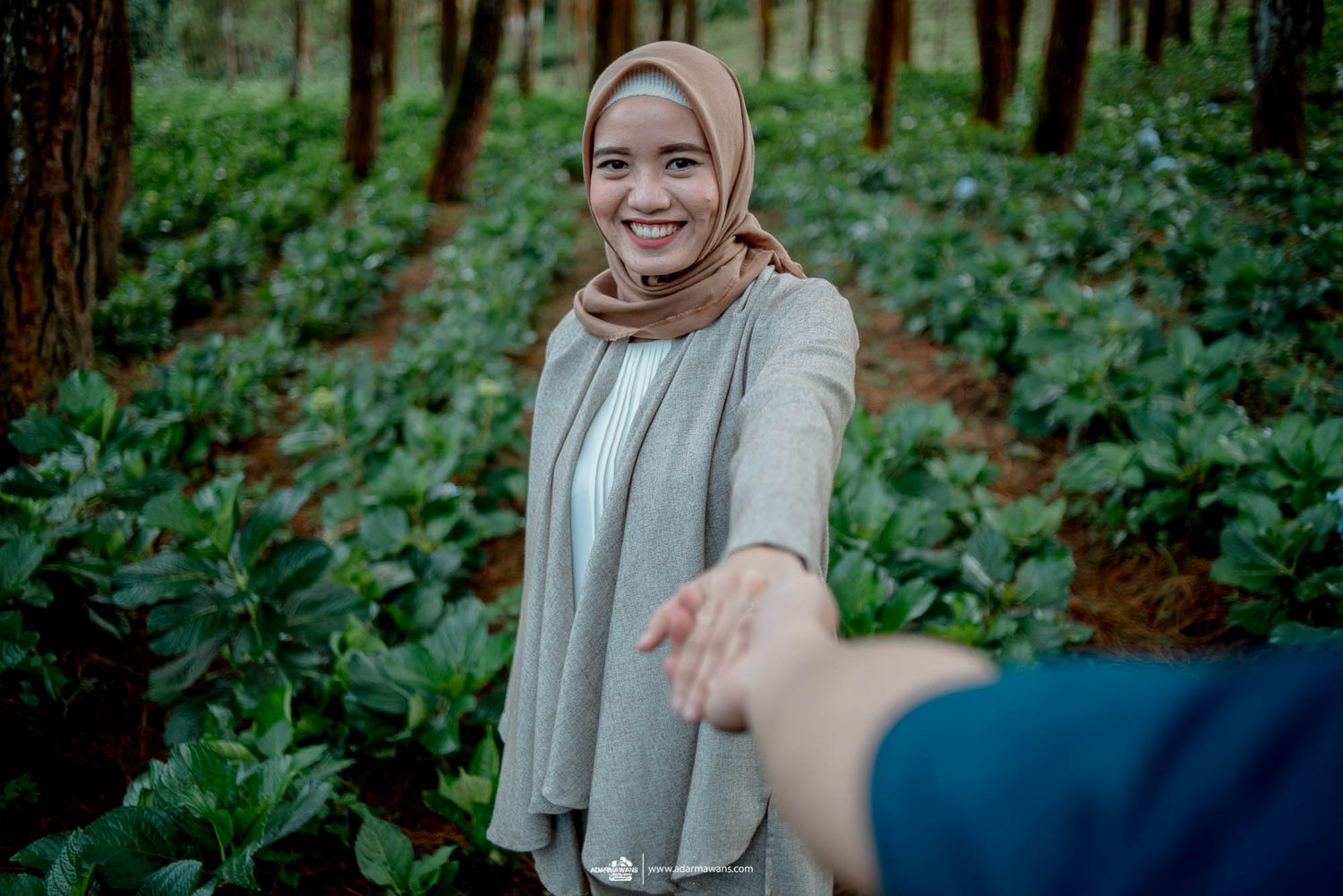 Person in light colored clothing reaching out playfully in a forest setting.
