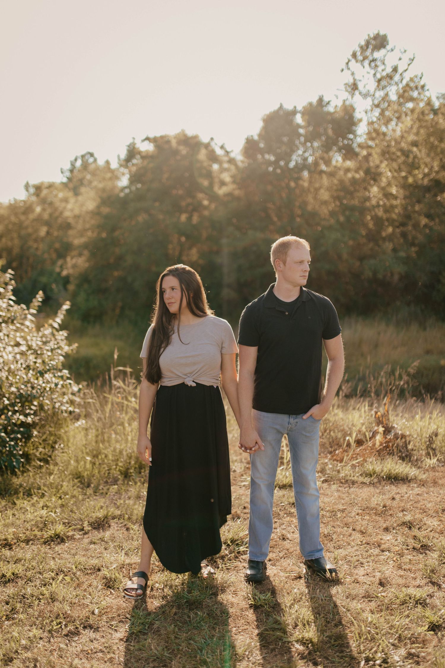 Couple poses together in a golden field during sunset.