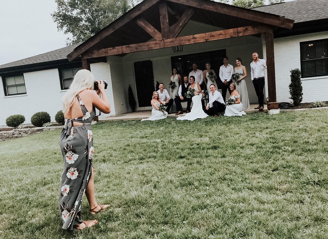 A photographer captures a group photo outside a rustic white building.