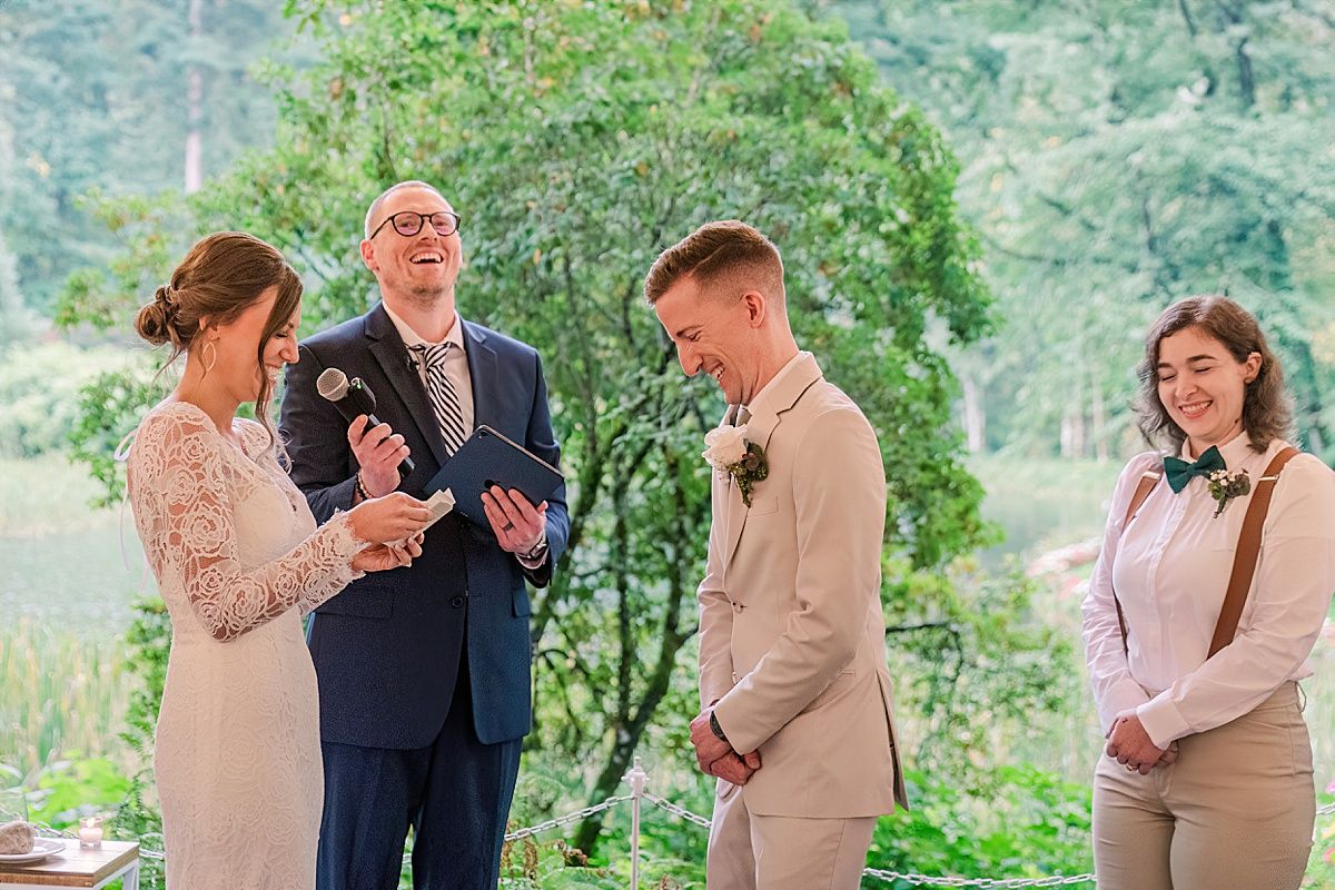 Joyful groom laughing while bride reads vows during wedding ceremony