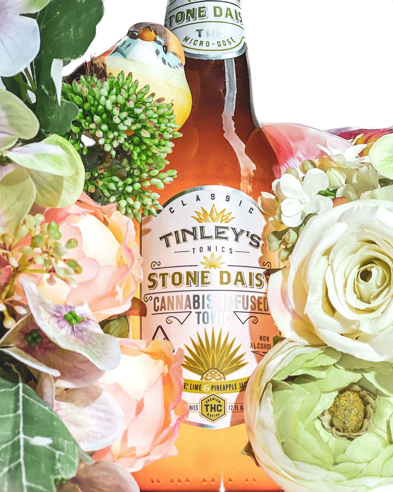 Tinleys Stone Daisy cannabis-infused tonic bottle surrounded by fresh pastel flowers and greenery.