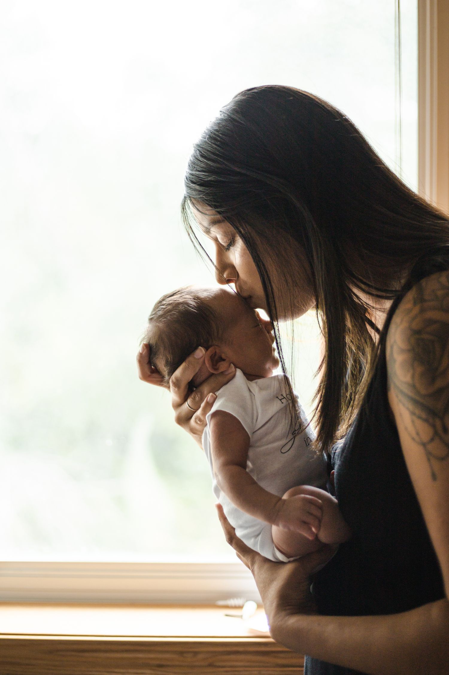 A tattooed mother kissing her newborn baby on the forehead.