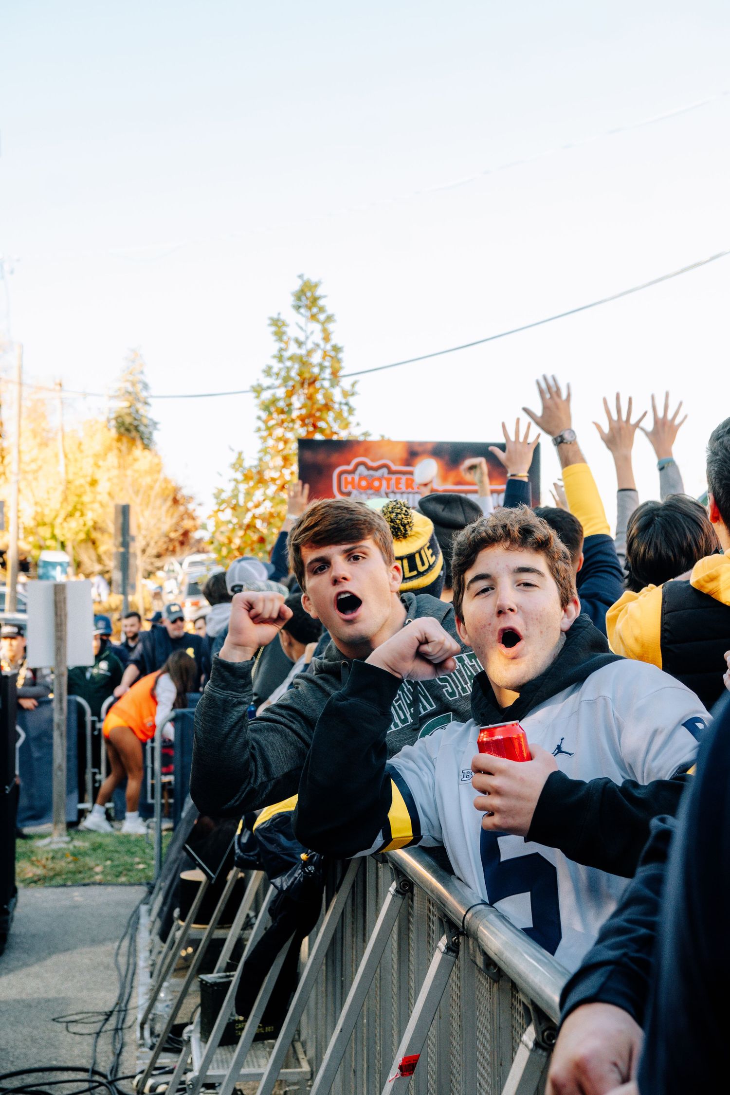 Excited young fans cheering and raising hands at a sporting event behind crowd barriers.