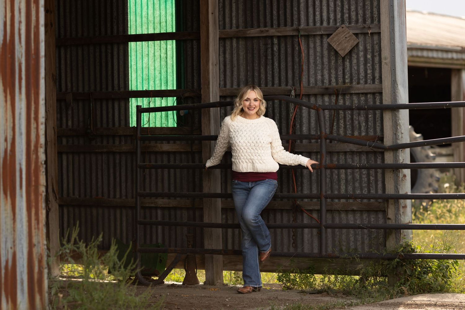A farmer's daughter leans against farm tube gates on her family cattle farm.