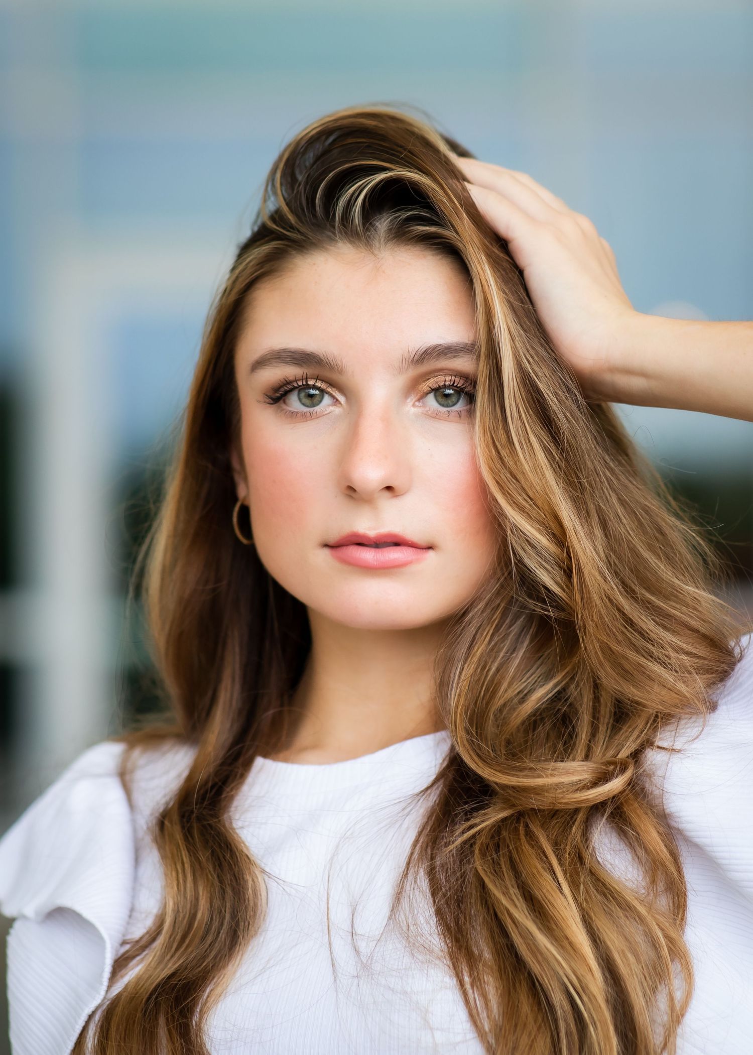 Professional portrait of a woman with flowing caramel-colored hair wearing a white top against a soft blurred background.