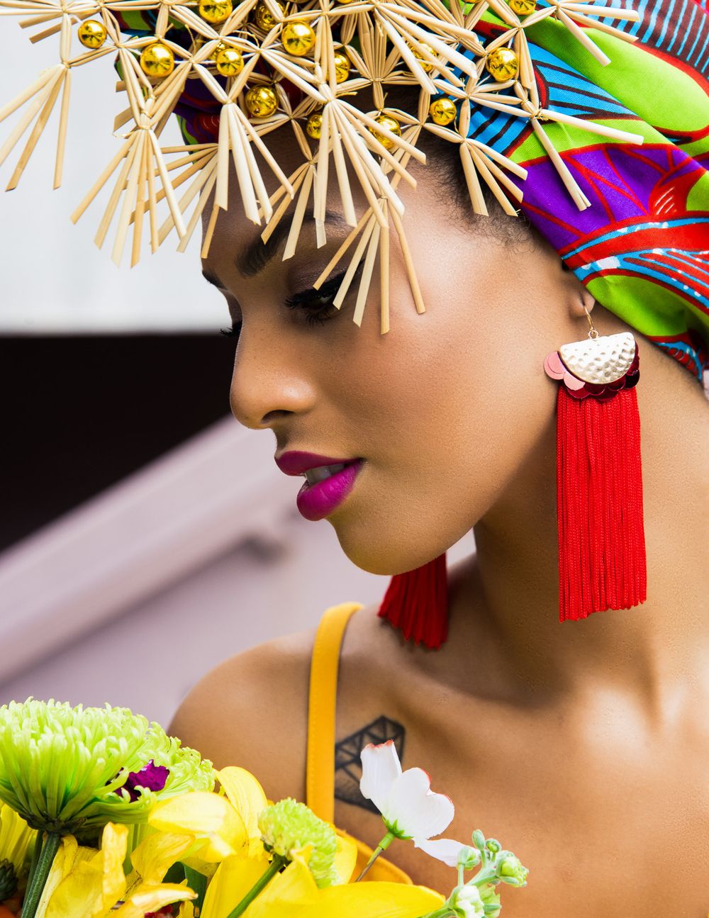 Creative fashion portrait with straw sunglasses and bright red tassels among yellow flowers.