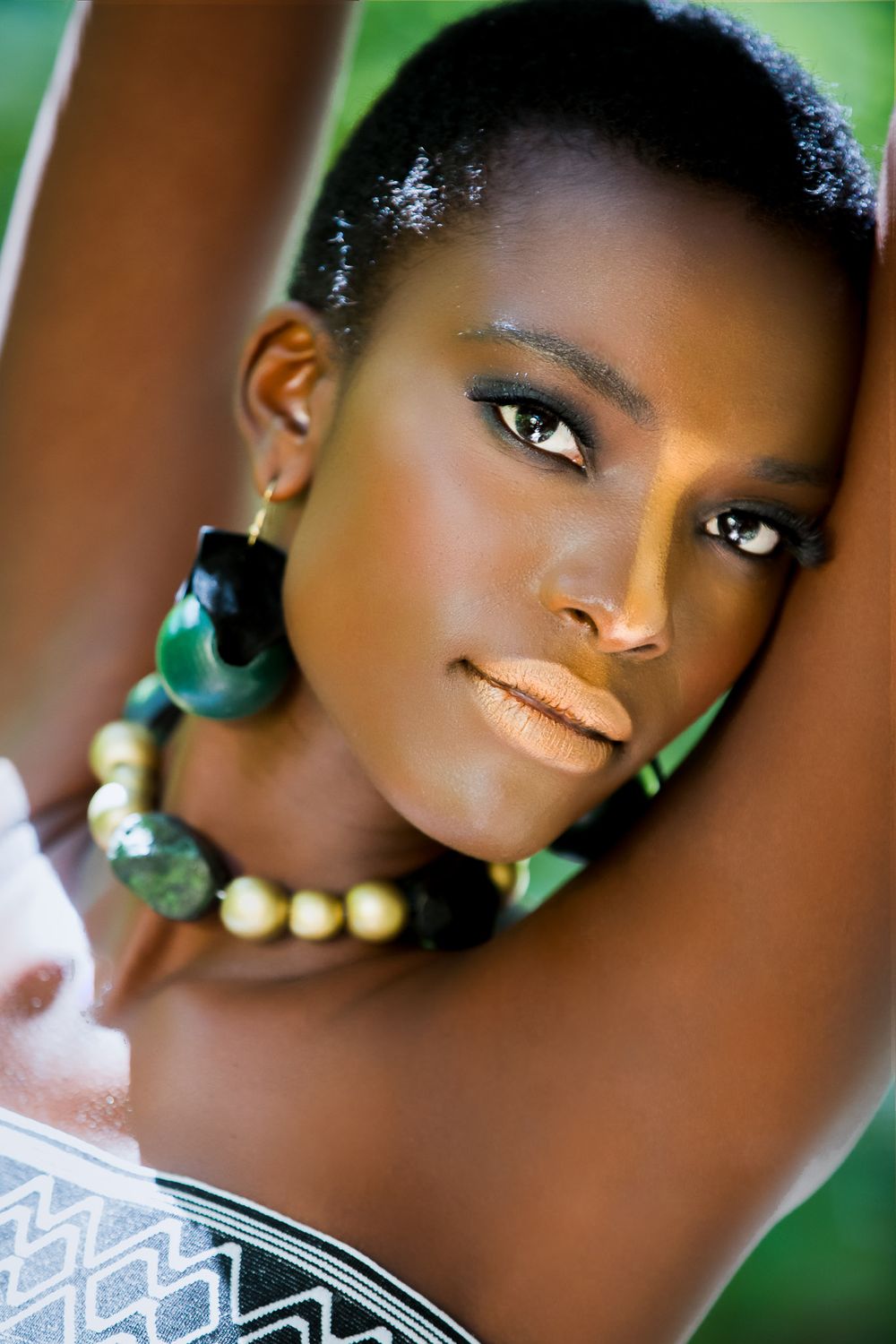 Portrait with green and gold statement jewelry against blurred background.