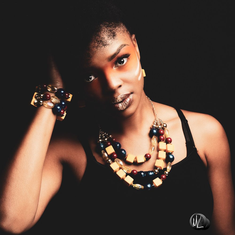 Dramatic low-key portrait with chunky beaded necklace against black background.