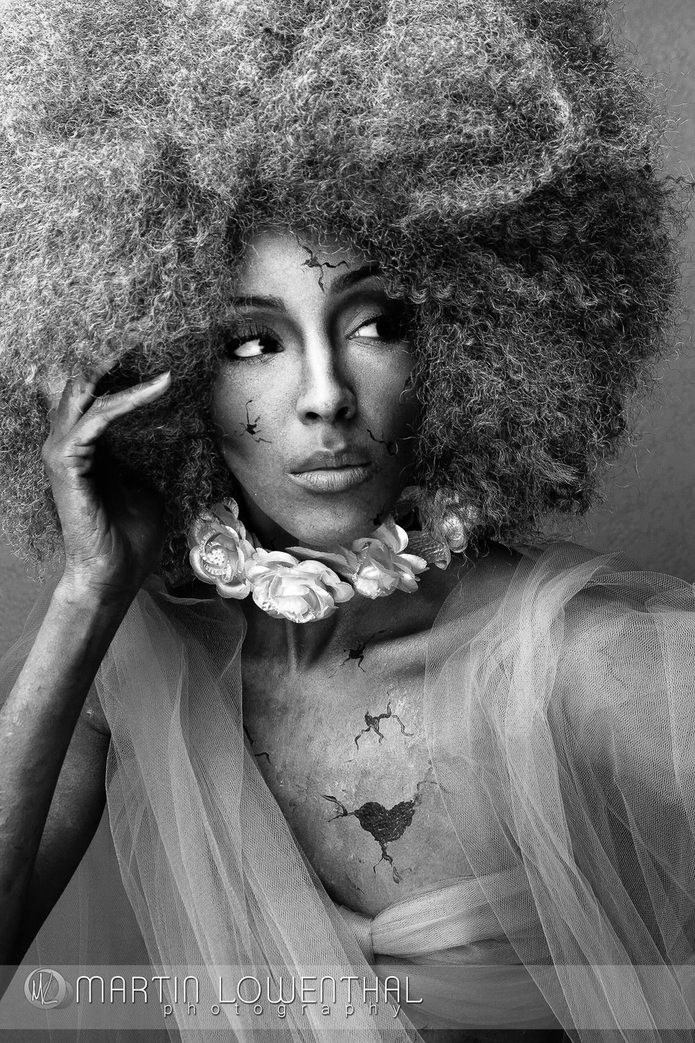 Artistic black and white portrait with dramatic afro hairstyle and floral accessories.