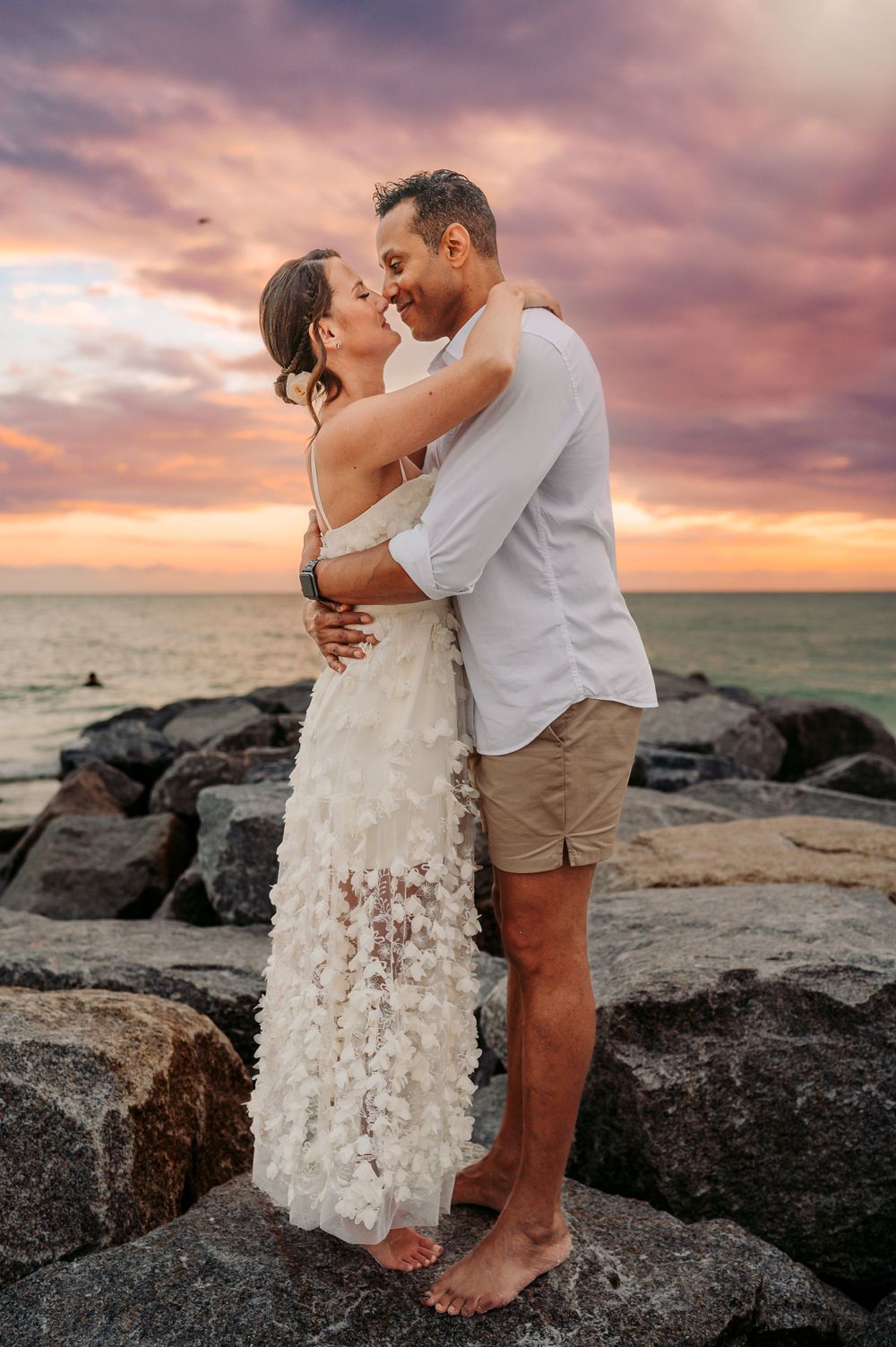 Couple standing in front of the soft waves at the beach at sunset.