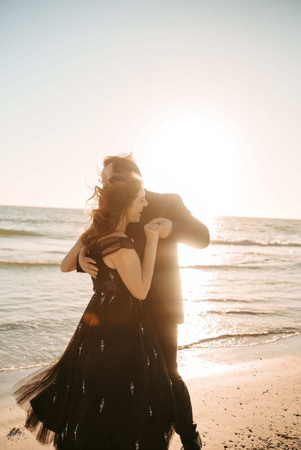 Man and woman dancing on the beach with the sunset in the distance.