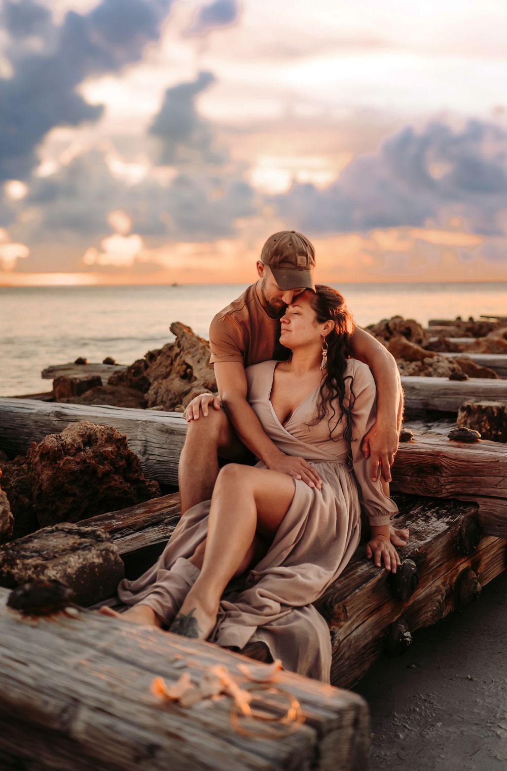 Man sits on the beach with his wife in his lap, while the wind is blowing their hair.