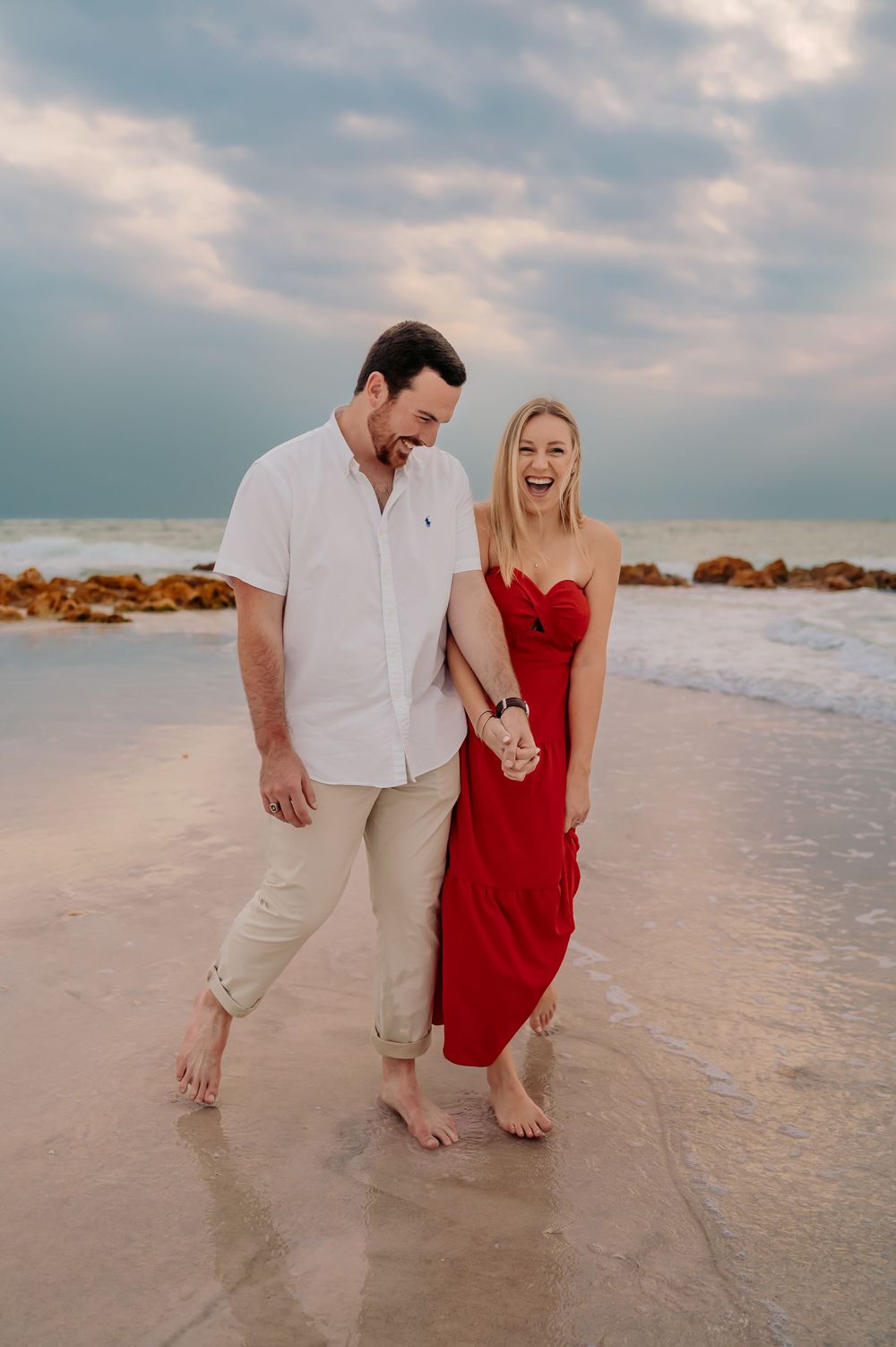 Man and woman walking on the beach, holding hands and looking at each other.