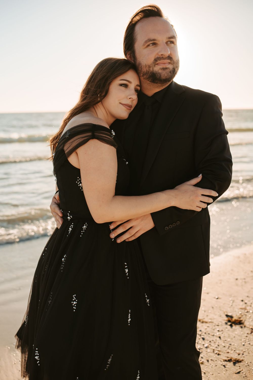 Woman leans on her husband's shoulder as they look down the coastline at the beach.