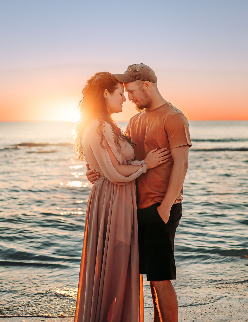 Man and woman face to face on the beach with the sunset behind them.