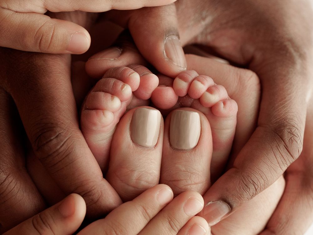 Close up of tiny baby feet cradled in gentle hands with neutral manicured nails.