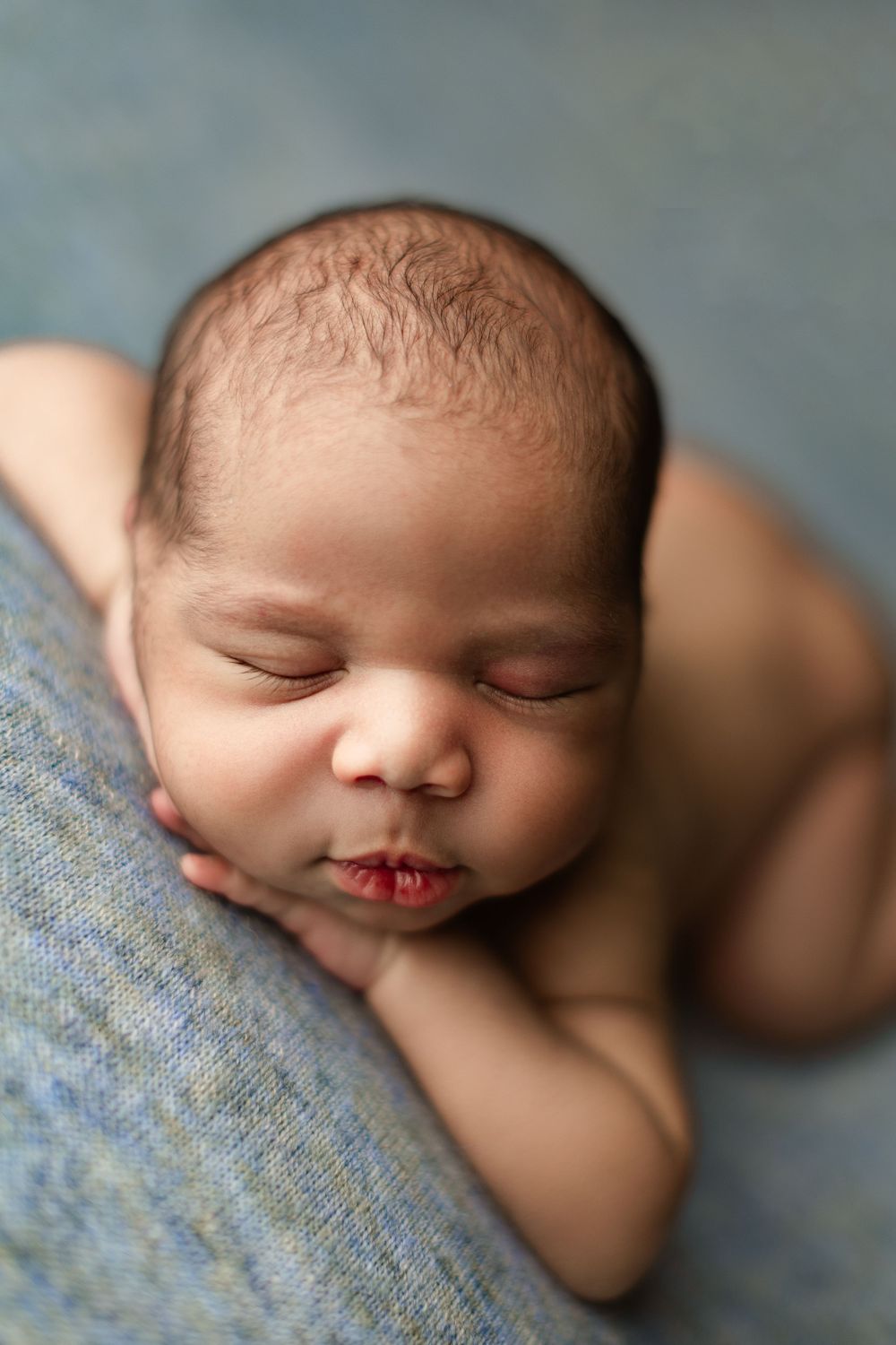 Sleeping newborn baby resting peacefully on blue blanket with tiny lips pursed in close-up portrait.