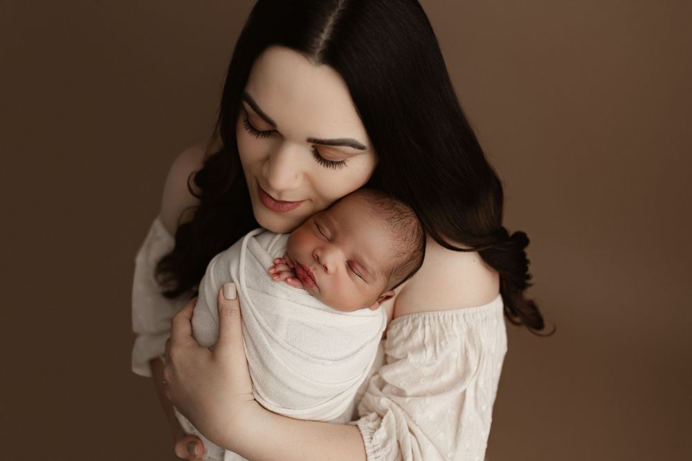 An intimate portrait of mother and newborn in soft lighting against brown backdrop.