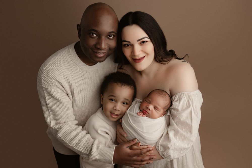 A beautiful family studio portrait with everyone dressed in white against brown backdrop.